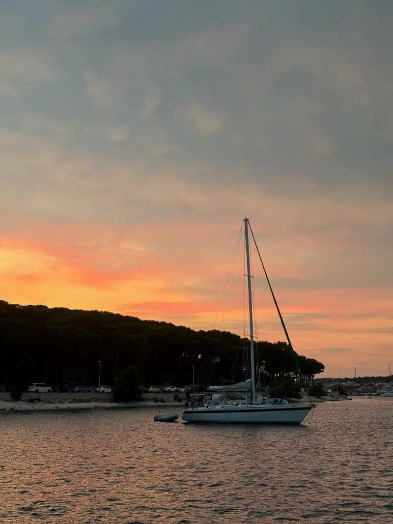 Sailboat silhouetted against an orange sunset at a quiet anchorage